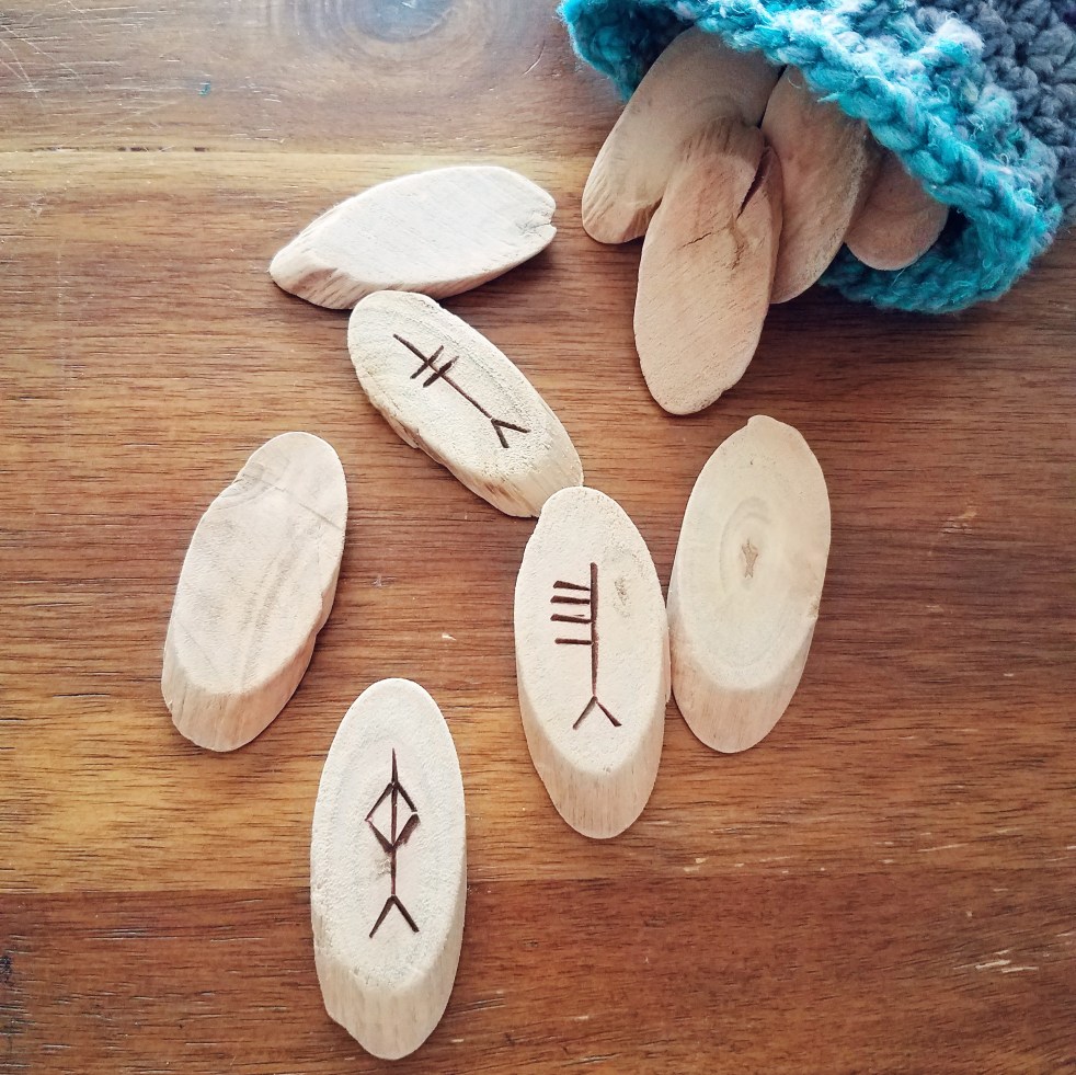 A set of driftwood Ogham staves spilling from a turquoise and grey pouch.