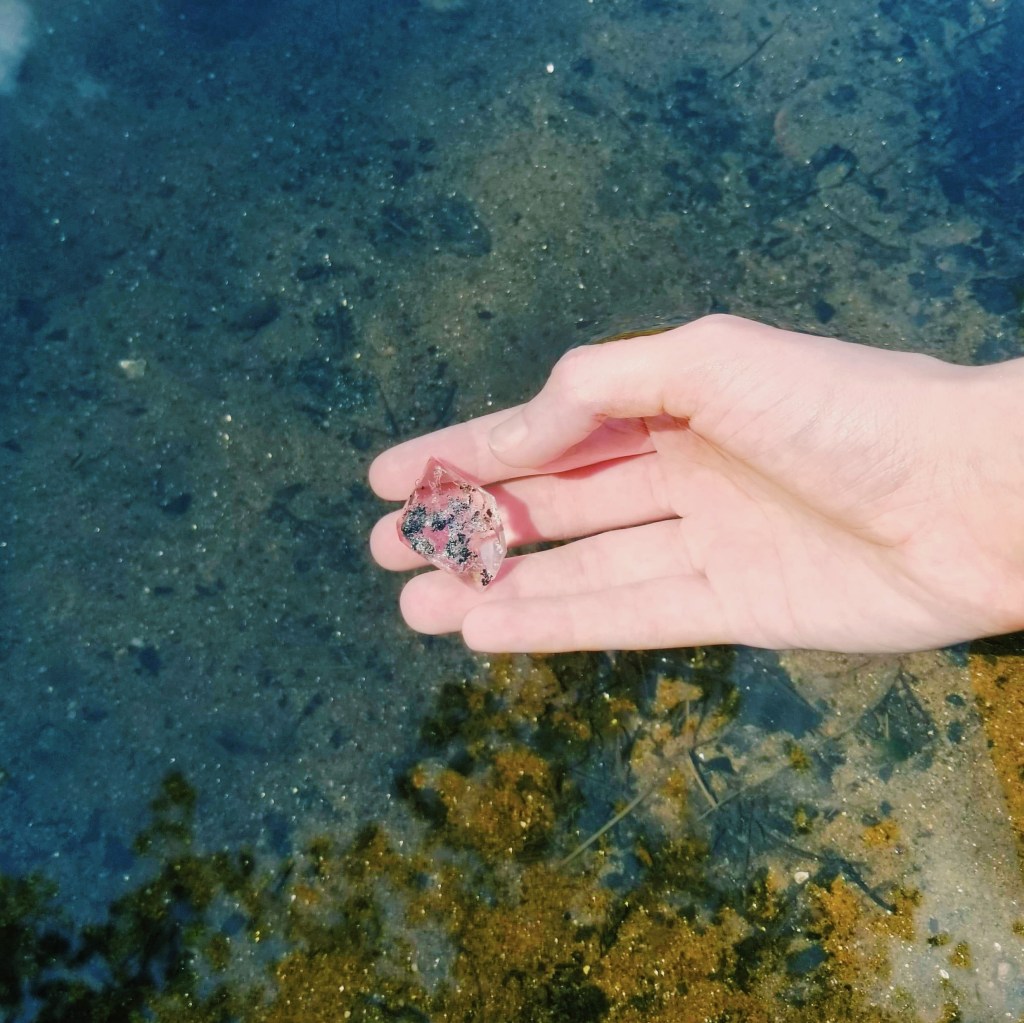 A hand holds a Herkimer diamond in clear river water.