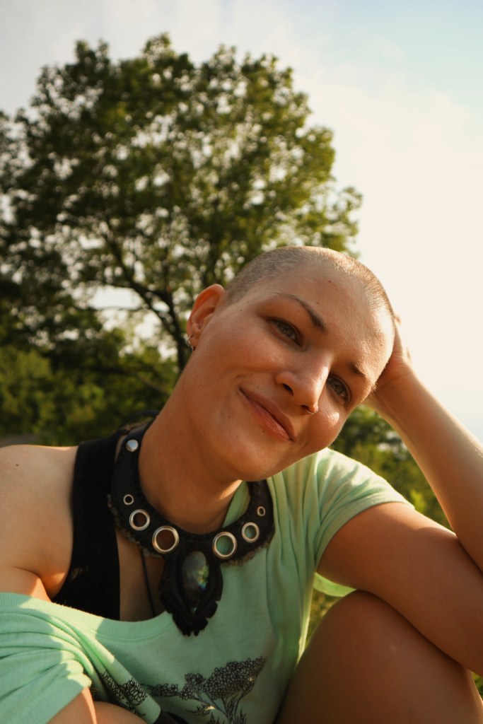A photo of me, sitting in front of a tree. My head is completely shaved. 