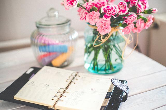 A vase of flowers and jar of chalk next to an open day planner.