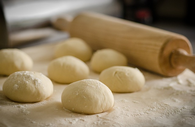 A rolling pin and several balls of biscuit dough on a floured board. 