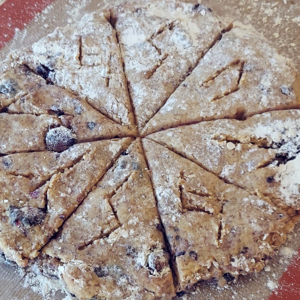 Unbaked blackberry scone dough, formed into a circle, cut into triangles, and inscribed with the runes jera, sowilo, teiwaz, uruz, algiz, and laguz.
