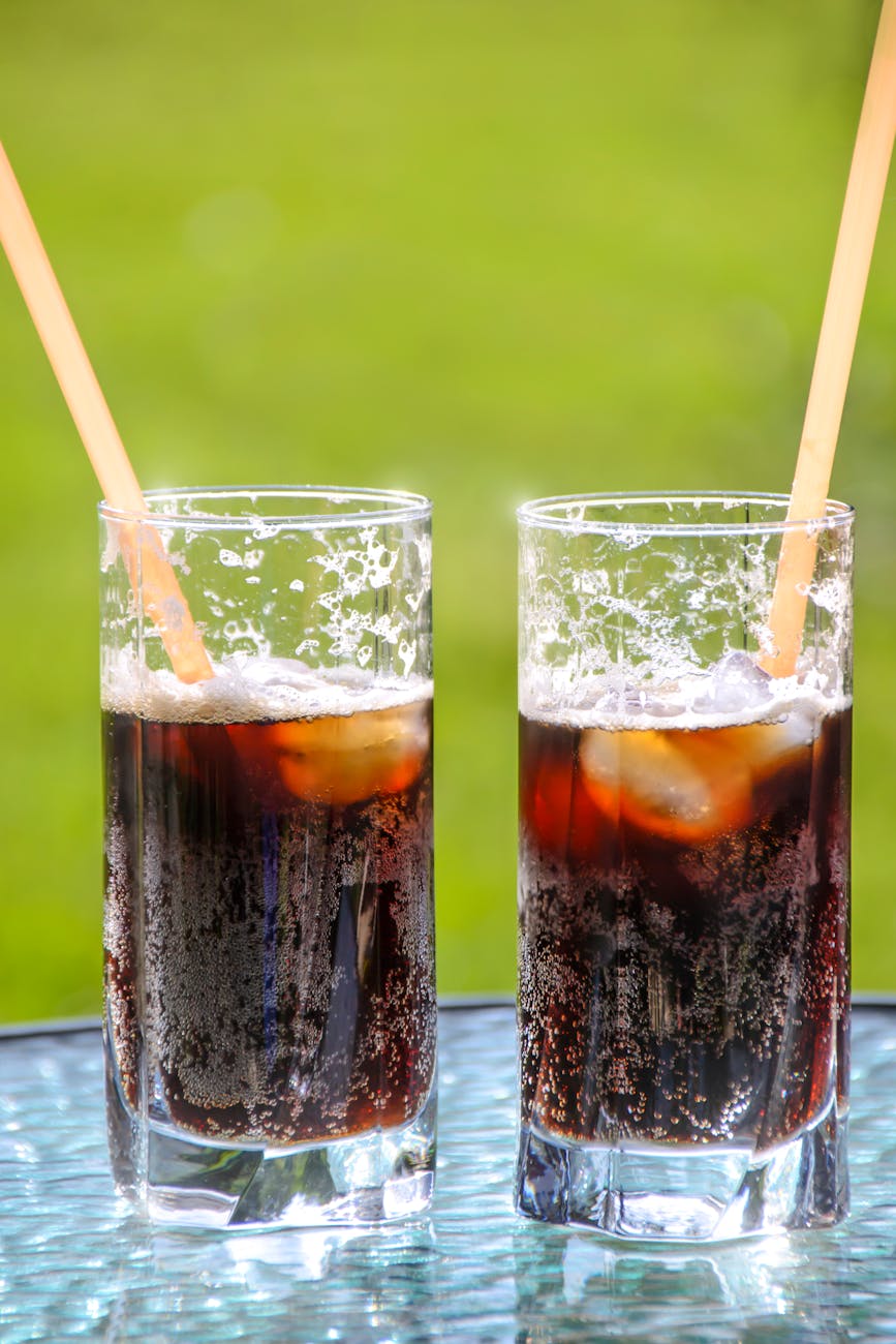Two glasses of soda, with ice and straws.