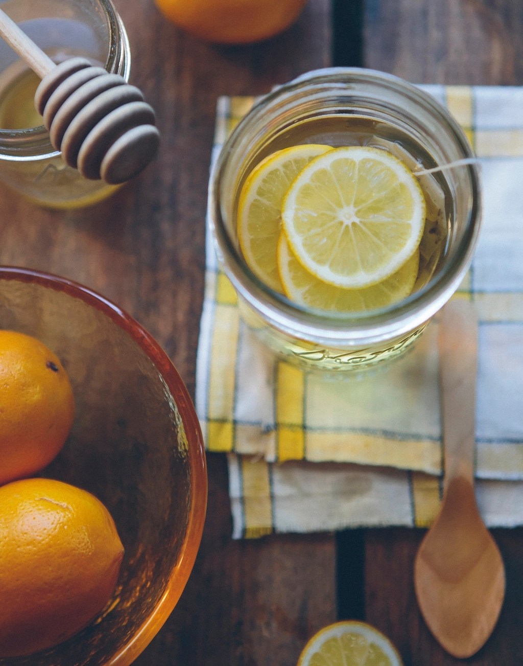 A jar of lemon tea, sitting atop a yellow and white napkin on a wooden table. 