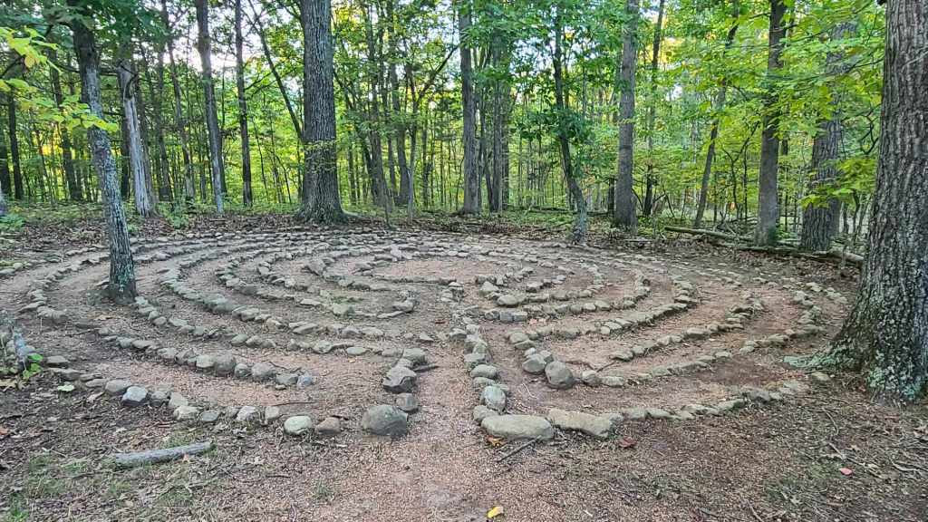 A photo of a labyrinth in a forest. The labyrinth is made up of stones, set in a spiraling pattern in a clearing. 