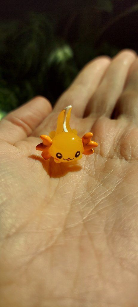 A tiny translucent orange axolotl sitting on the palm of a hand. 